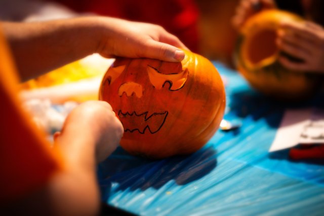 Kind schnitzt bei der Halloweenparty einen Kürbis mit aufgemaltem Gruselgesicht