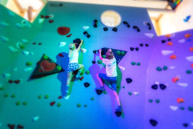 Zwei Kinder klettern an der bunt beleuchteten Boulderwand mit zahlreichen Klettergriffen