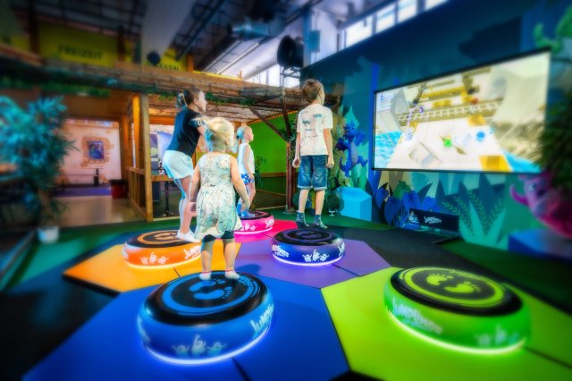 Kinder springen auf den leuchtenden Jump-Pots vor einem großen Bildschirm mit dem Jumplings-Spiel