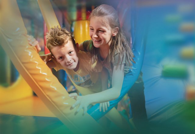 Blick auf den bunten Indoorspielplatz mit Klettertürmen, Rutschen und verschiedenen Spielgeräten